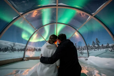Pareja en un iglú de cristal bajo la aurora boreal en un viaje de novios original